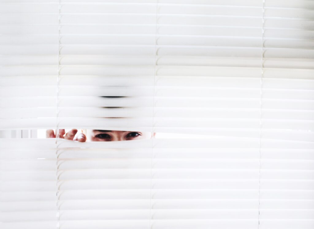 A police officer looks through the blinds of a home.